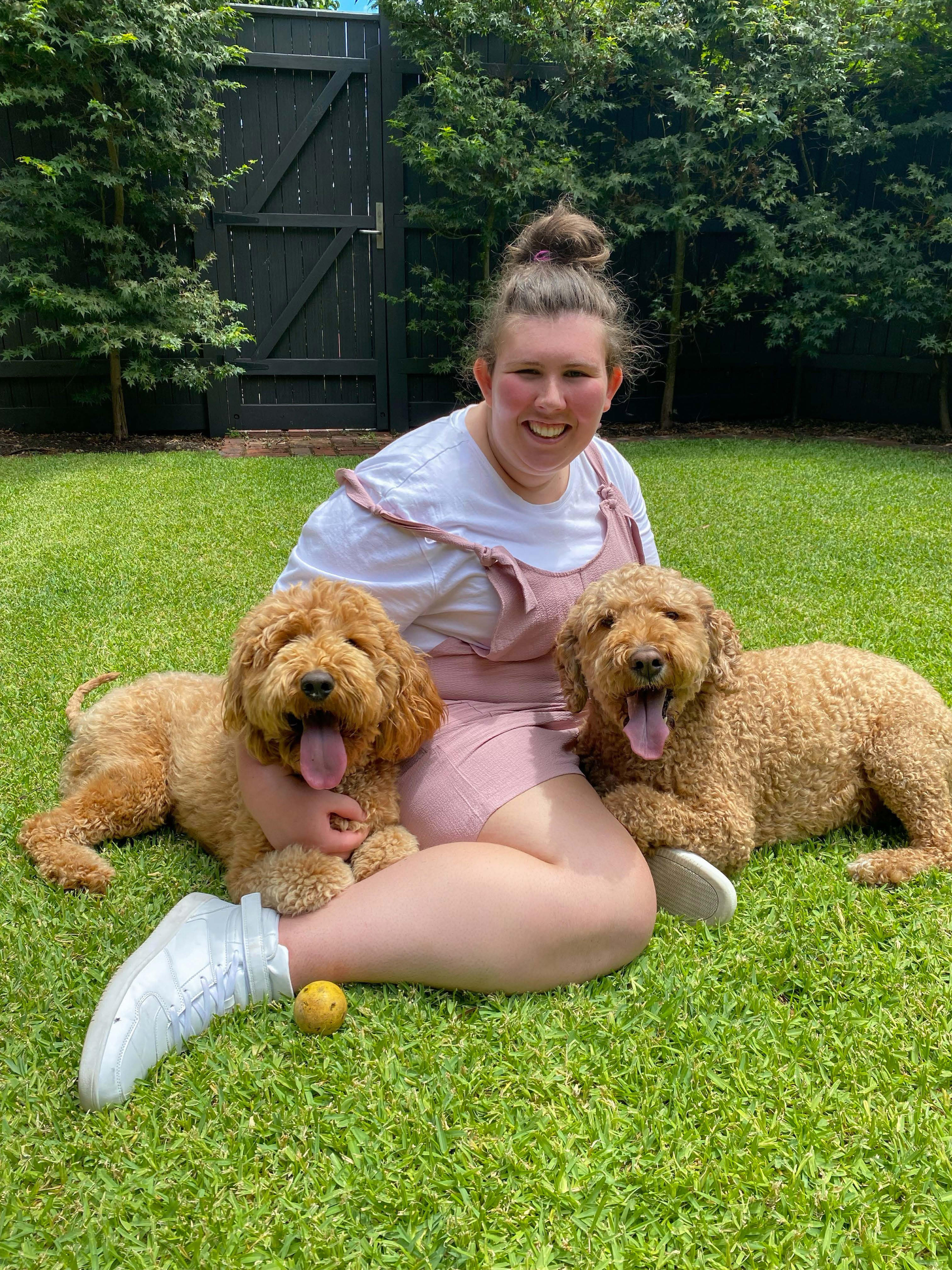 Jovem sentada na grama com dois cachorros