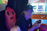 A man sits with a young boy in an arcade machine, playing a game.