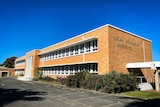Brick building with white window frames and horizontal features in a modernist rectangular frontage and empty car parks in front