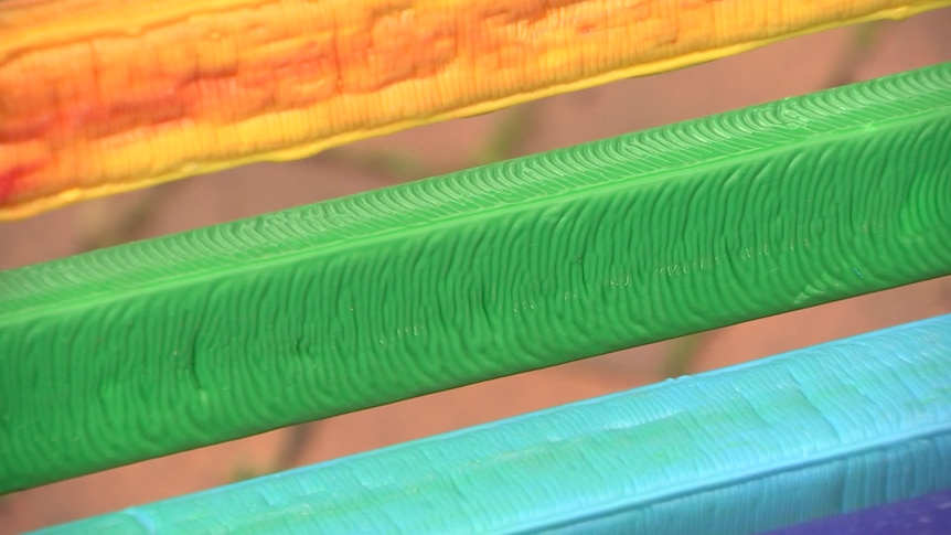 A close-up of a rainbow-coloured bench made from recycled plastic lids.