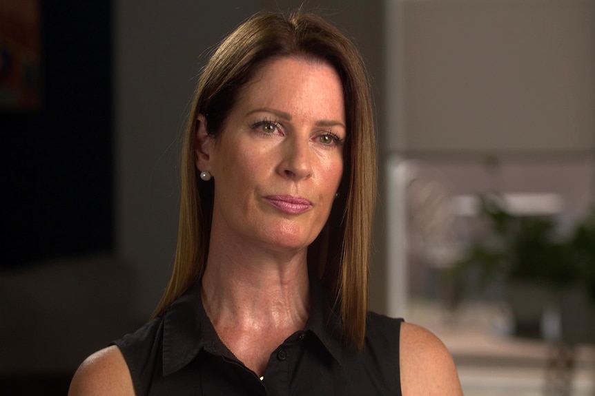 A woman with long brown hair and a neutral facial expression.