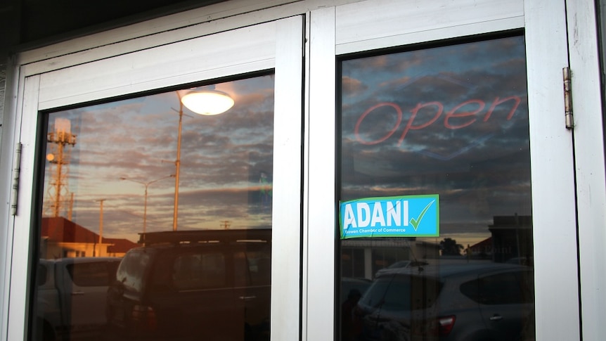 A glass shop door with an Adani yes sticker and a sunset in the background