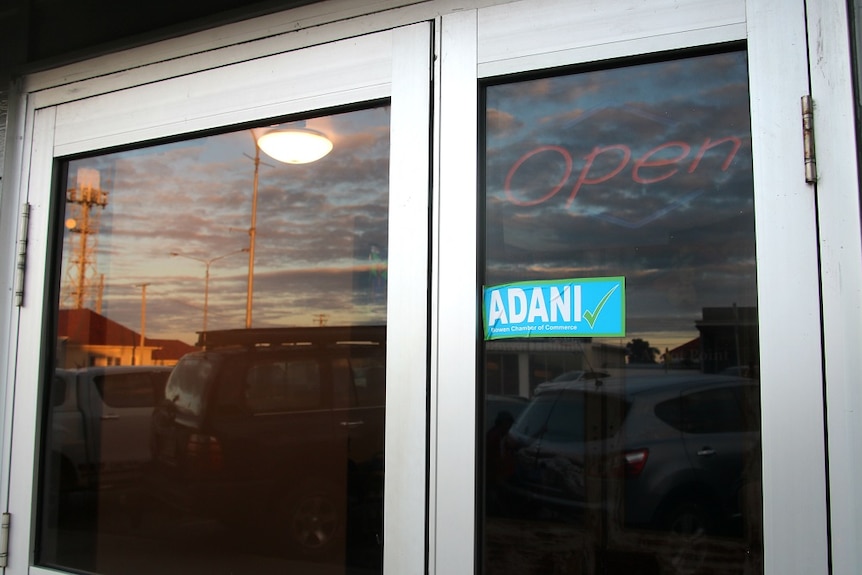 A glass shop door with an Adani yes sticker and a sunset in the background.