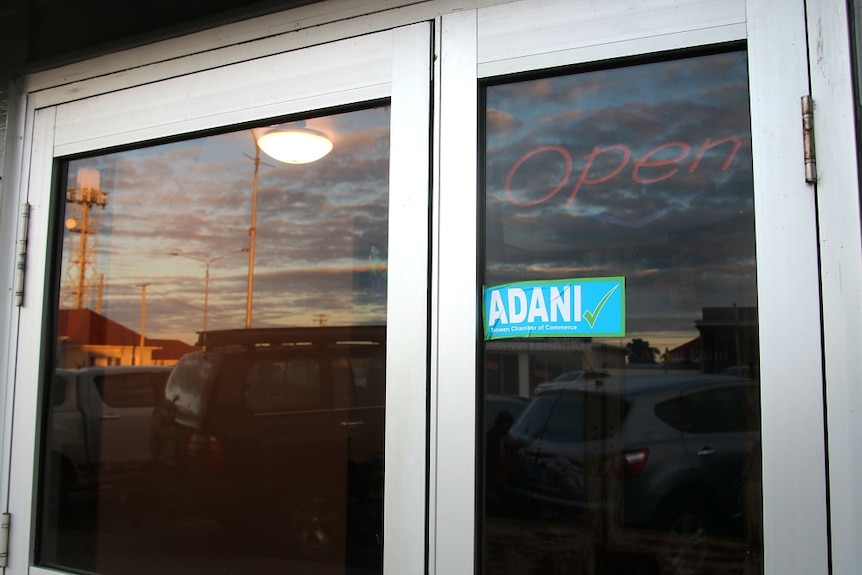 A glass shop door with an Adani yes sticker and a sunset in the background