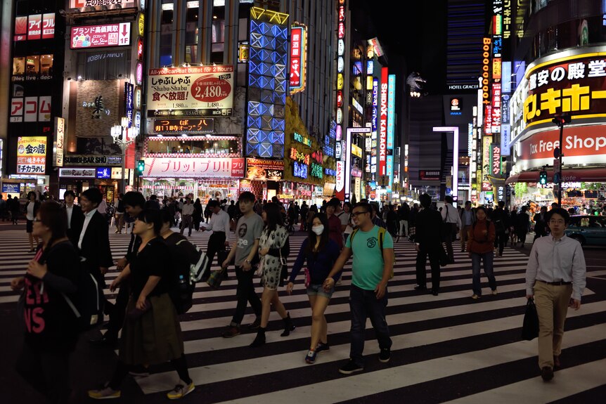 People cross a major intersection in Tokyo at night.