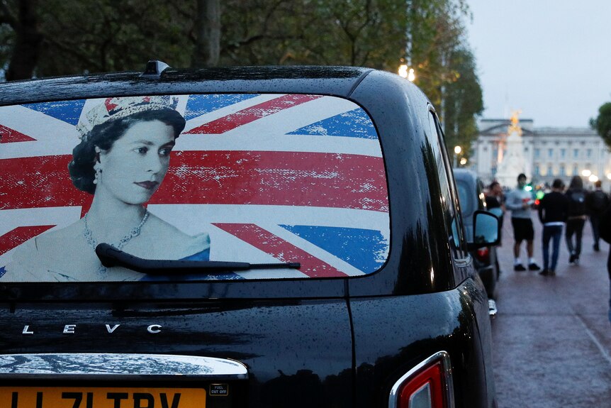The rear window of a cab with the image of Queen Elizabeth on it.