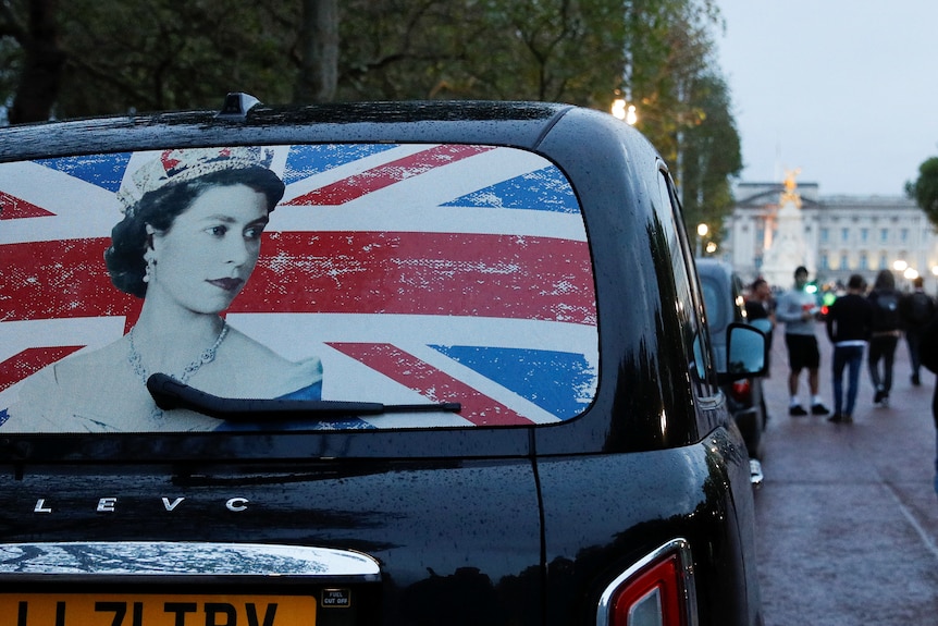 The rear window of a cab with the image of Queen Elizabeth on it.