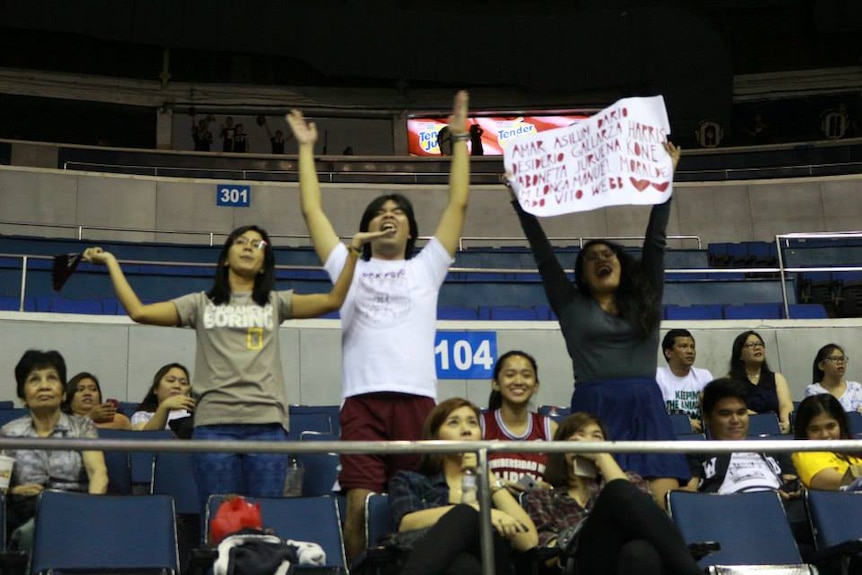 Three people in a stadium with signs cheering