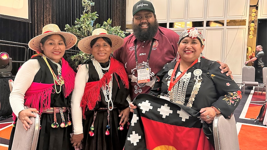 A tall indigenous australian man with three short indigenous Chilean women.