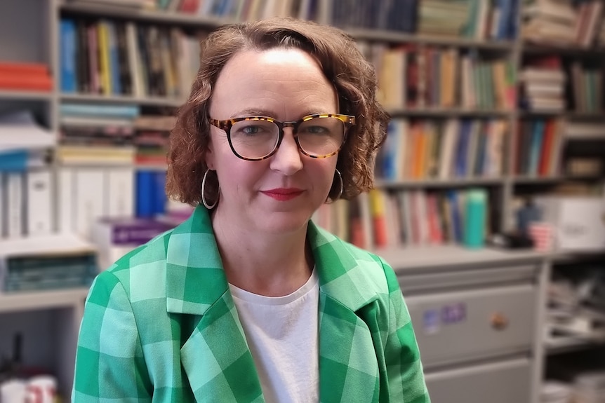 Close up of a woman wearing a green check blazer and glasses.