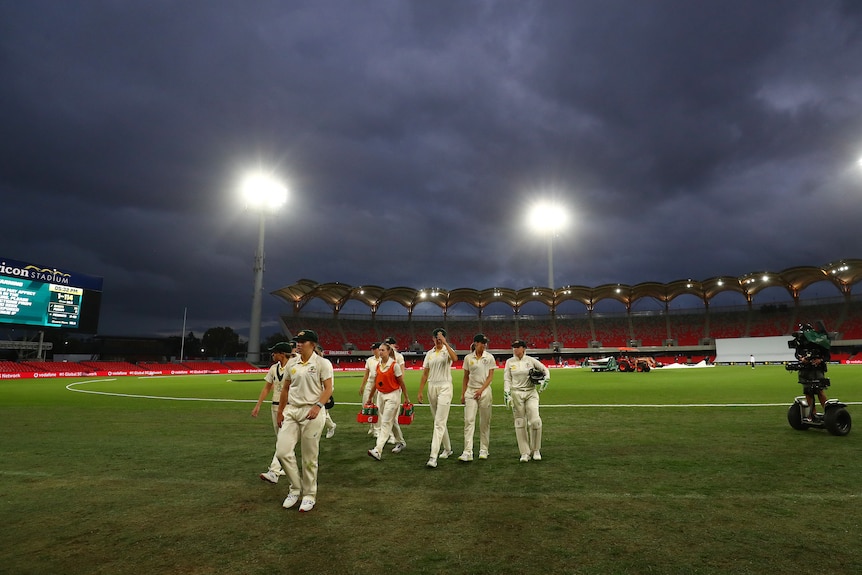The floodlights shine on the field as clouds loom over the Australian players