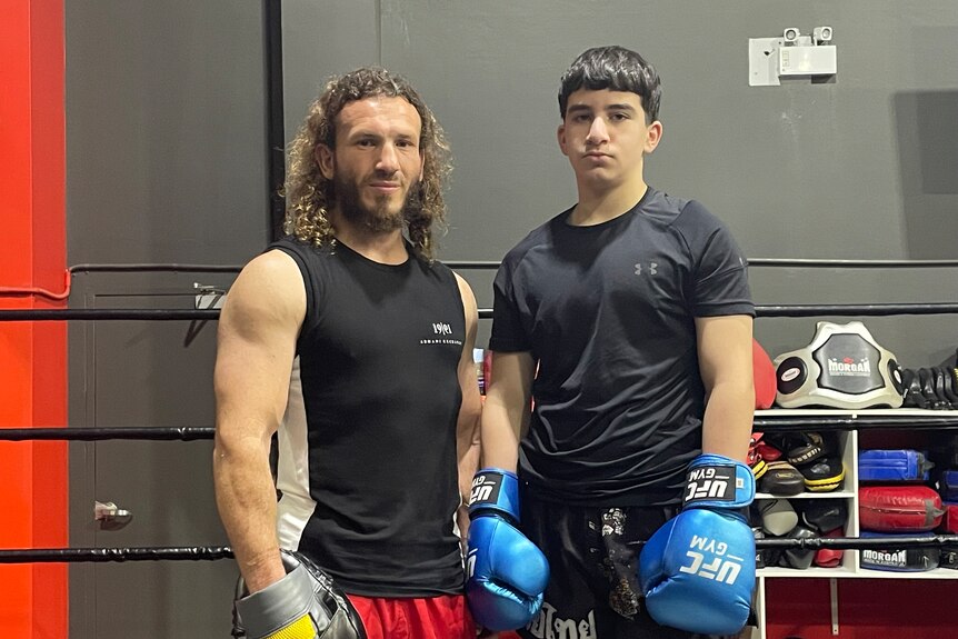 Un homme et un adolescent se tiennent dans un ring de boxe avec des gants