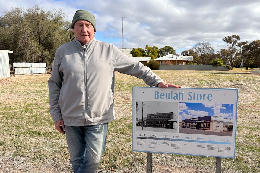 A man standing next to a sign in front of an empty block of land.