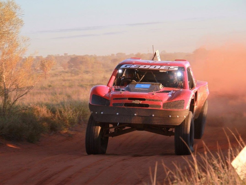 A red truck races through the Finke Desert, with red dust blowing behind