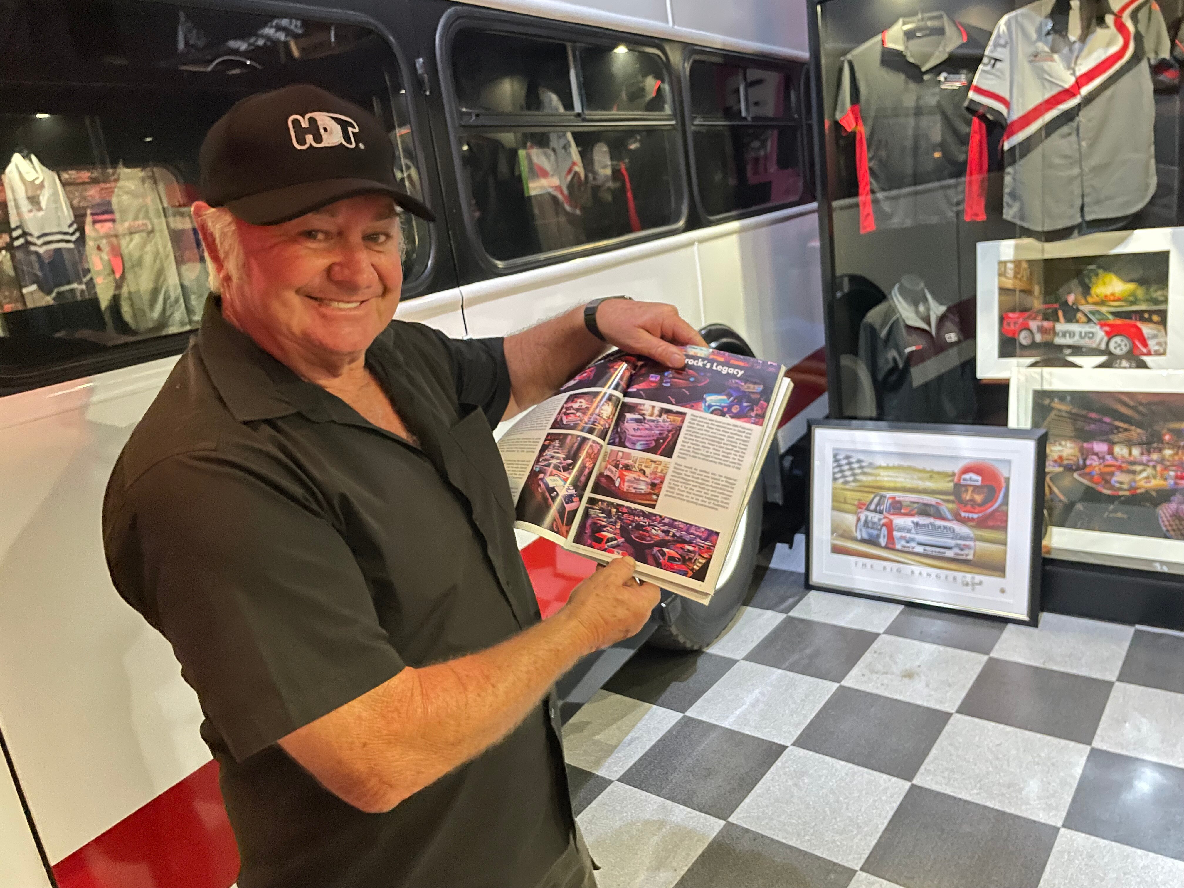 Racing fan Peter Champion points to a Peter Brock book with memorabilia behind him.