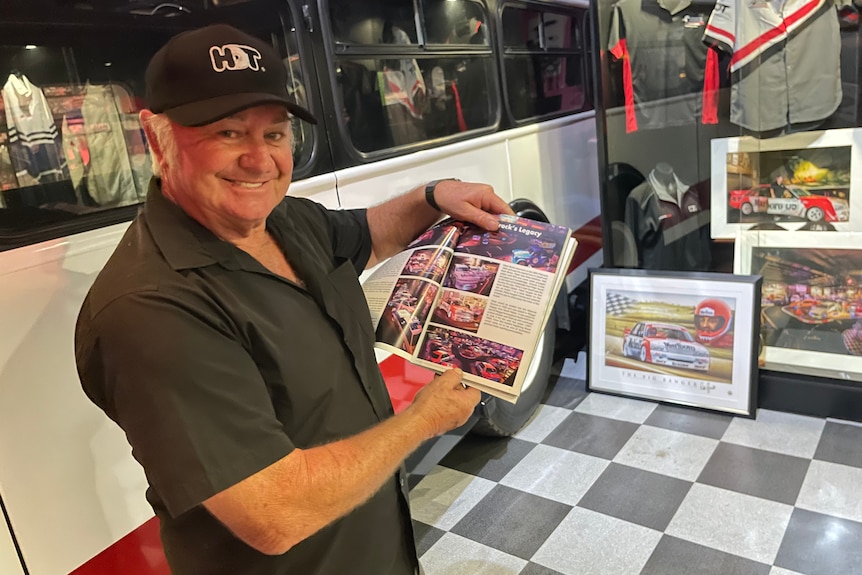 Racing fan Peter Champion points to a Peter Brock book with memorabilia behind him.