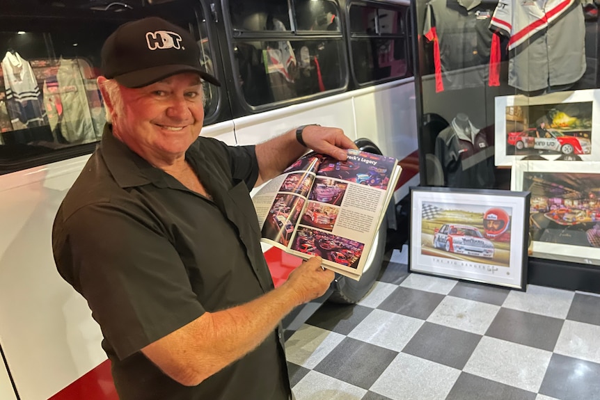 Race fan Peter Champion points to a Peter Brock book with memorabilia behind him.