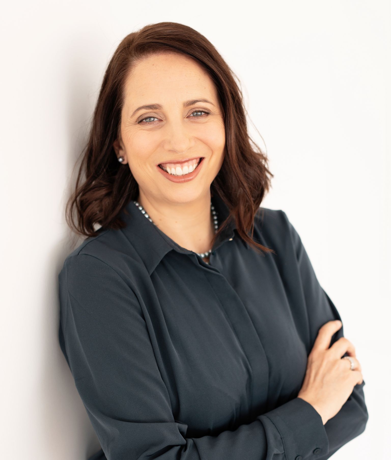 A woman leaning against a wall smiling and looking at the camera