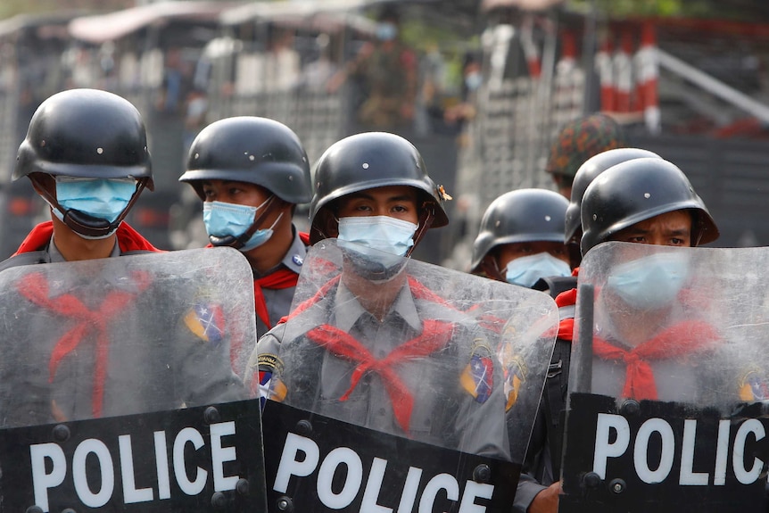 Riot police stand guard behind a road barricade in Mandalay