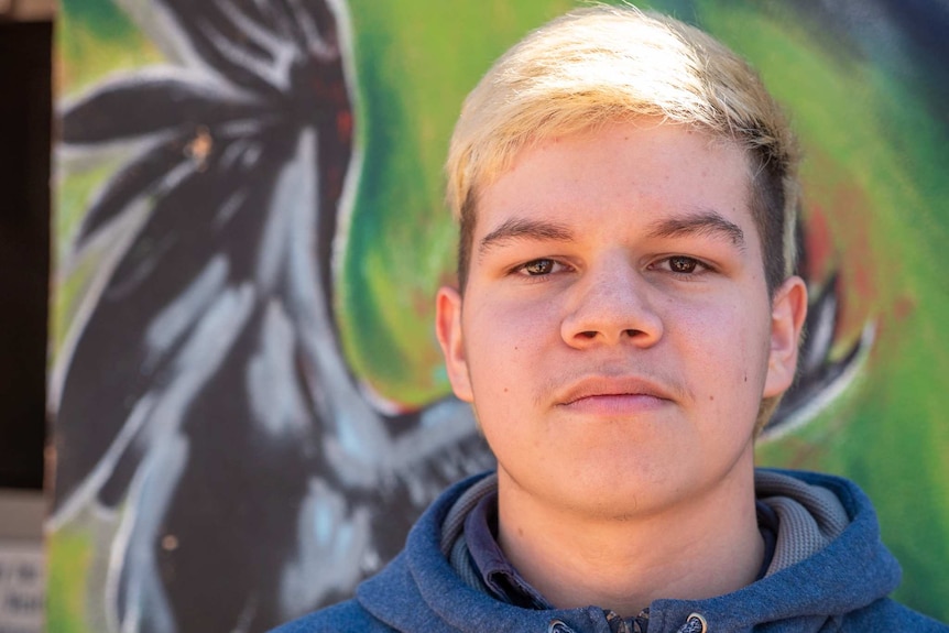 A young Indigenous man stands looking directly into the camera.