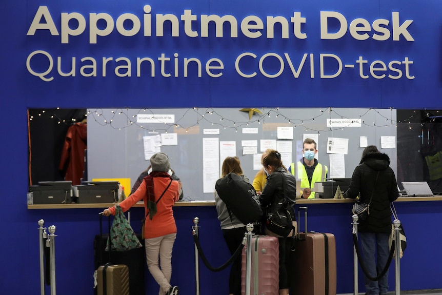 People wait in front of a desk at Schipol airport in Amsterdam marked "Appointment Desk" for COVID testing and quarantine. 