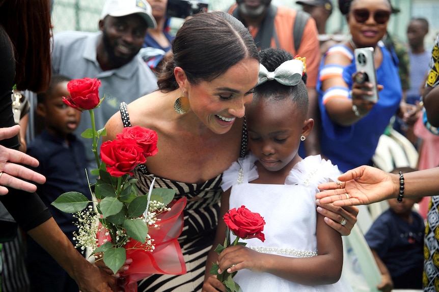 Meghan Markle smiles while hugging a child who gave her a bouqet of roses.