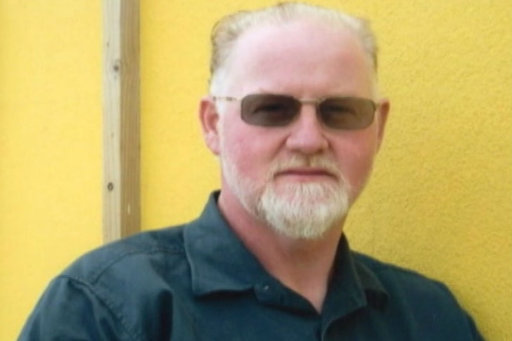 Craig Minogue wearing sunglasses in front of a yellow wall.