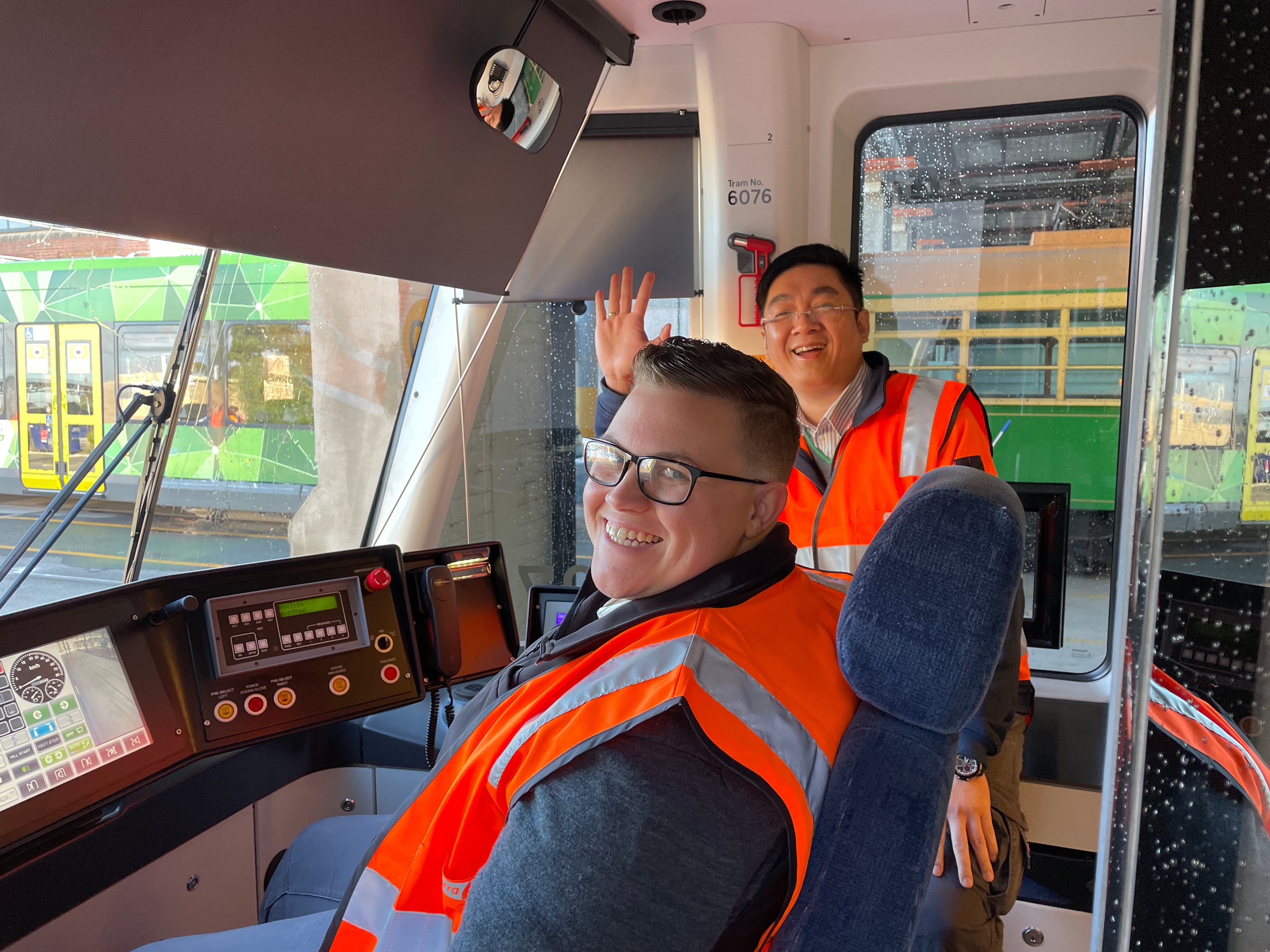 Two tram drivers in a tram cockpit smiling at the camera