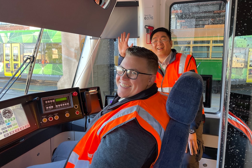 Two tram drivers in a tram cockpit smiling at the camera