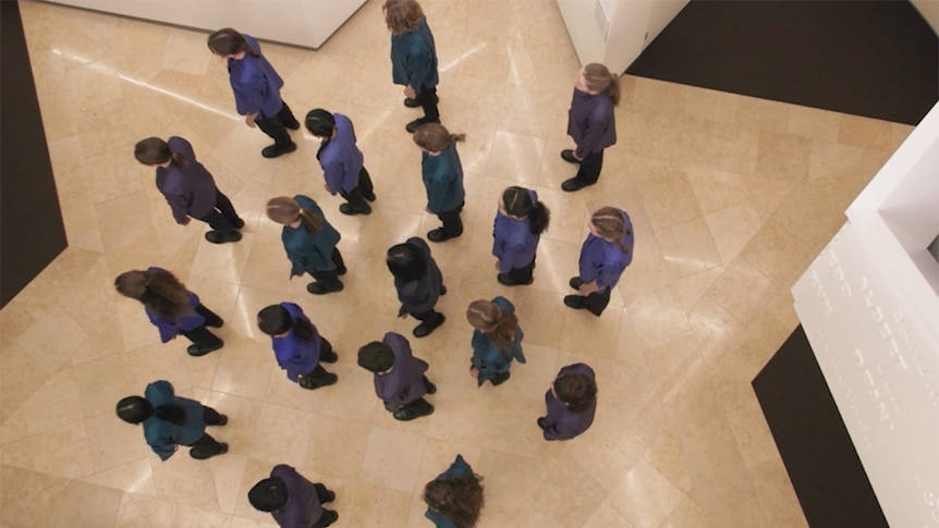 A group of singers shot from above standing in a star-shaped space in the Sydney Jewish Museum.