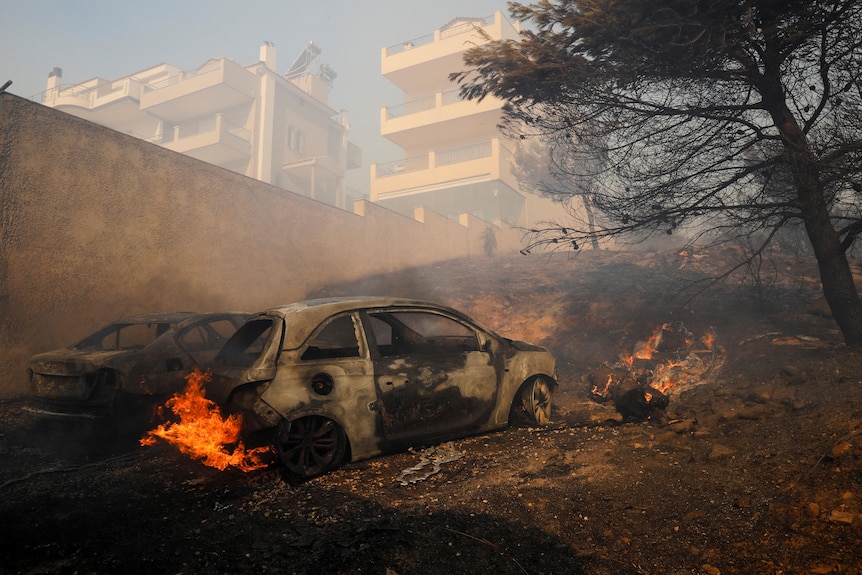 Un'auto in fiamme con le fiamme che salgono da dietro con sopra lo smog. 