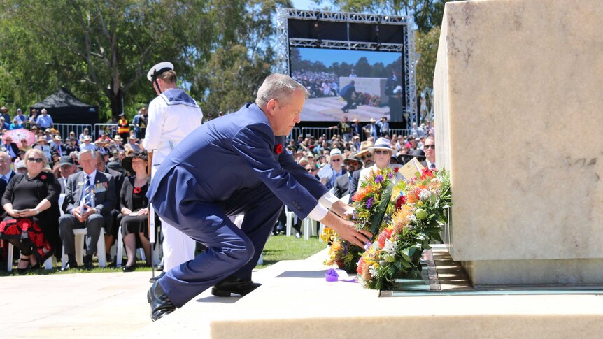 A man bends over to lay a wreath.