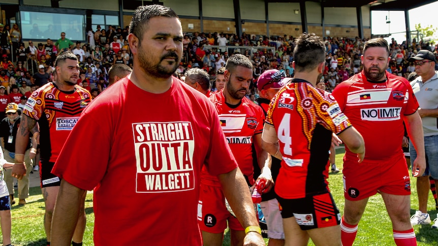 Aboriginal men walk onto Rugby League field wearing "straight outta Walgett" shirt