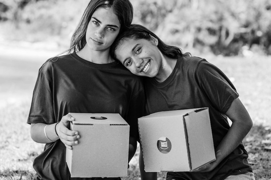 Two young indigenous girls holding a small cardboard box each.