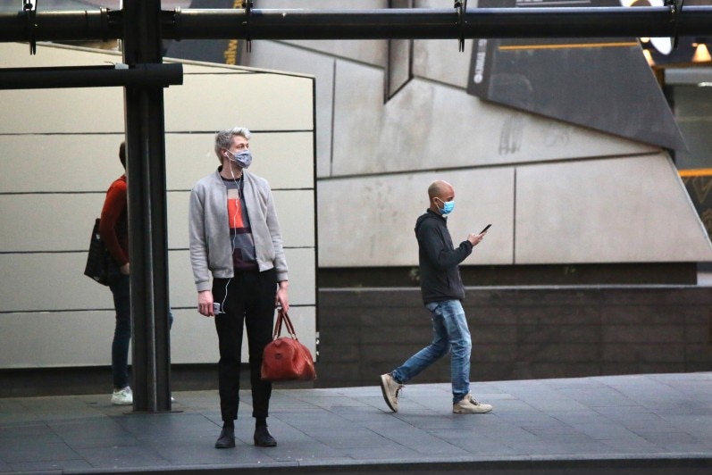 People with masks on at a bus stop.