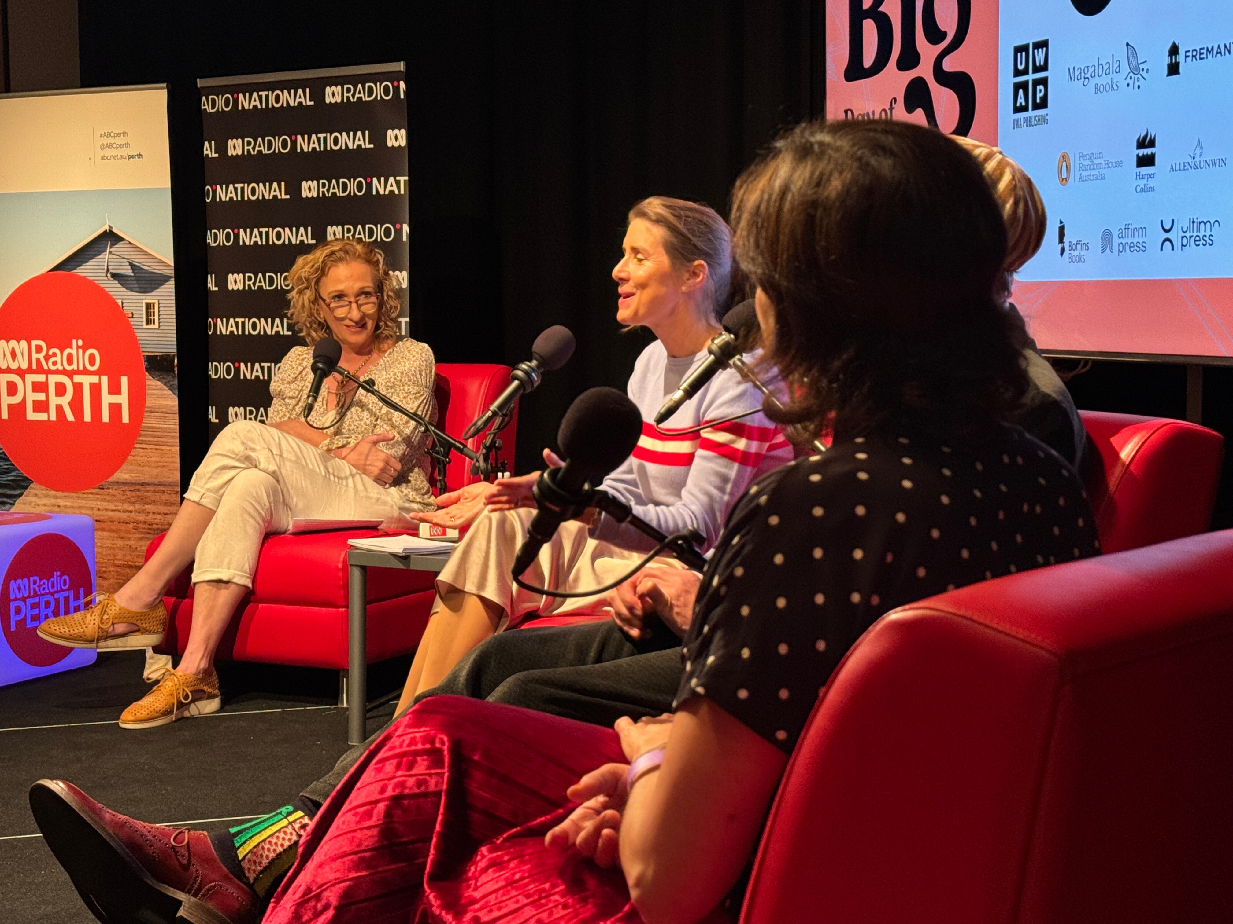A radio host with curly hair sits on a red chair talking to three authors on red chairs.