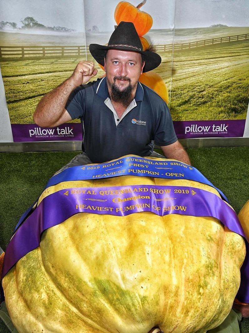 A man in a black hat sitting near a giant pumpkin