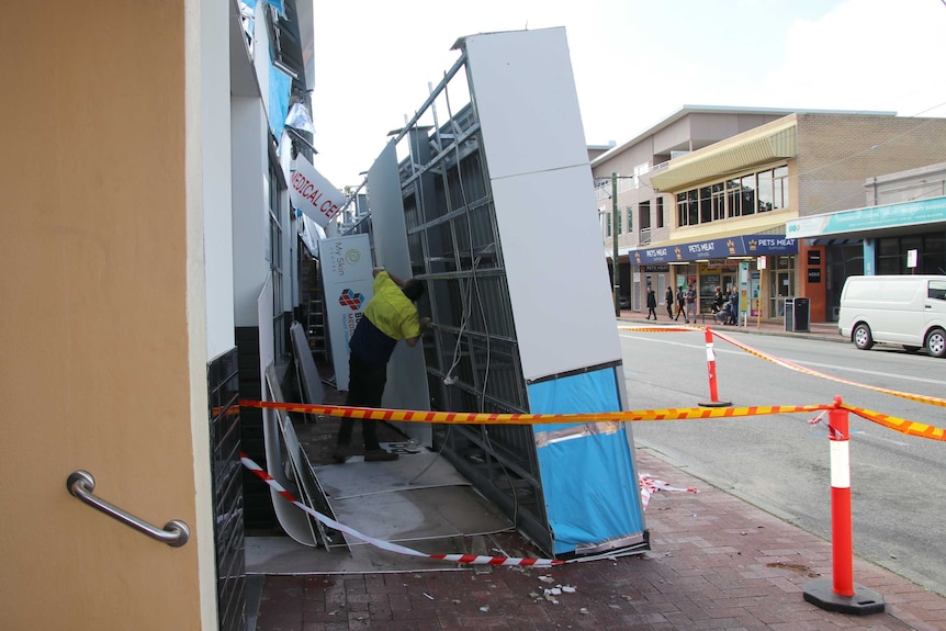 A man in a hi-vis shirt inspects an awning which sits sideways on a footpath in Mount Hawthorn after collapsing.