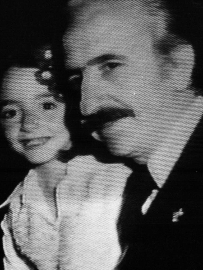 Black and white screenshot of a video showing a mustached man holding a little girl 