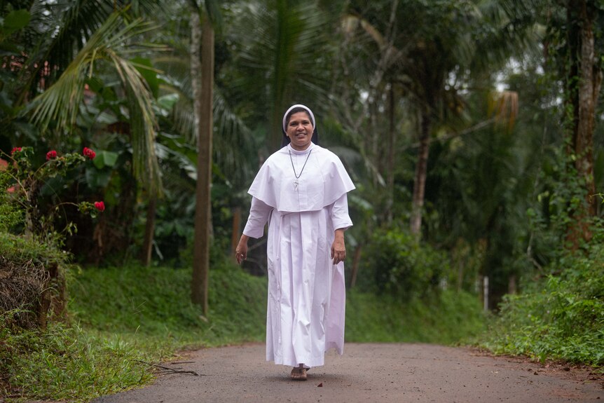 Sister Lucy Kalapura walks along a pathway lined by trees.