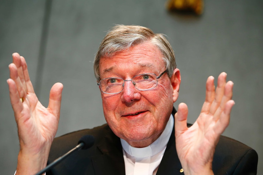 George Pell holds his hands up as he speaks.