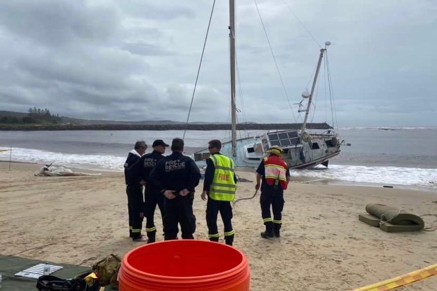 White yacht sits on beach shore line while rescue crews stand beside it on the sand