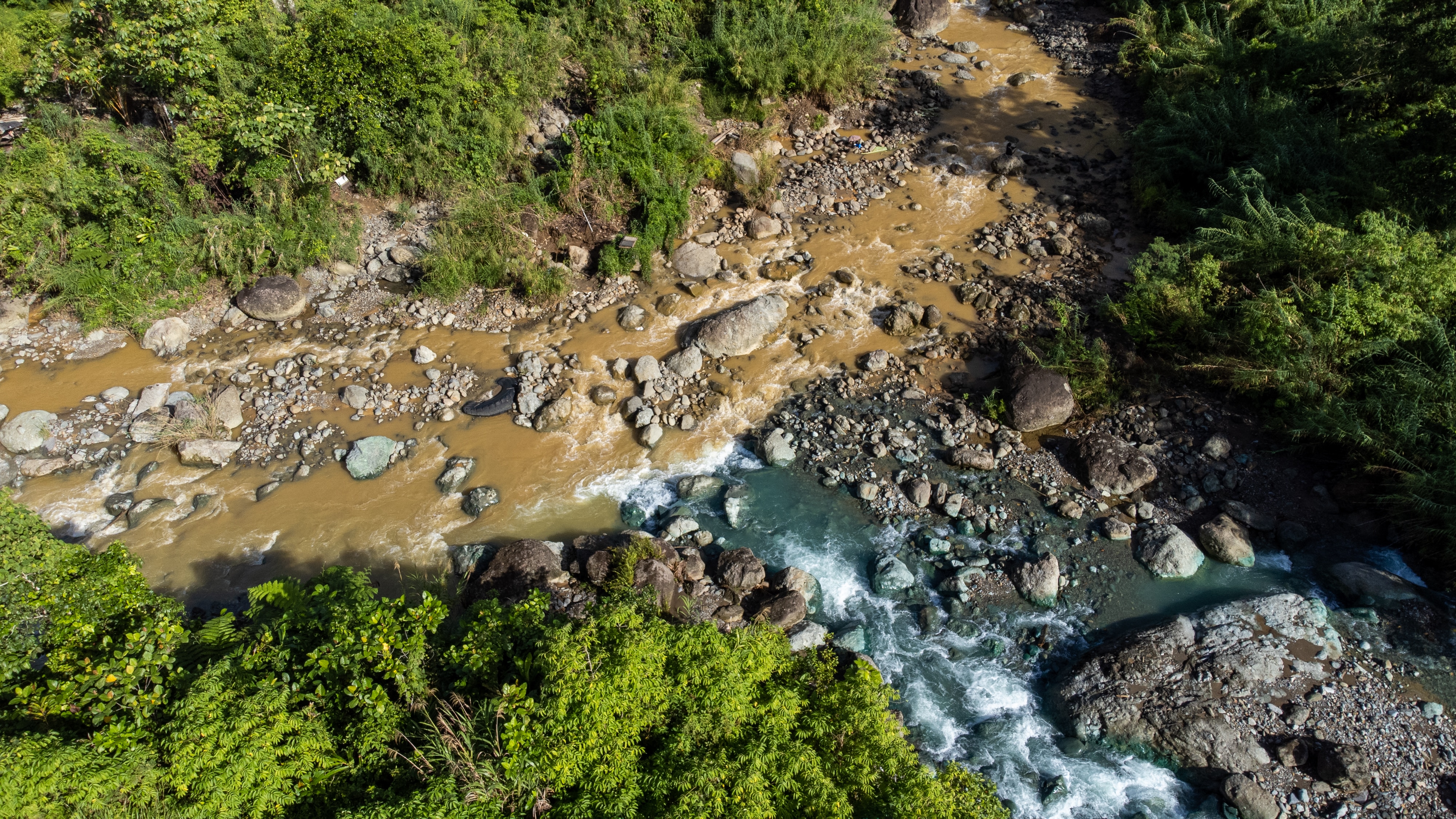 A birds eye view of a flowing brown coloured river meeting with a blue tinged river.