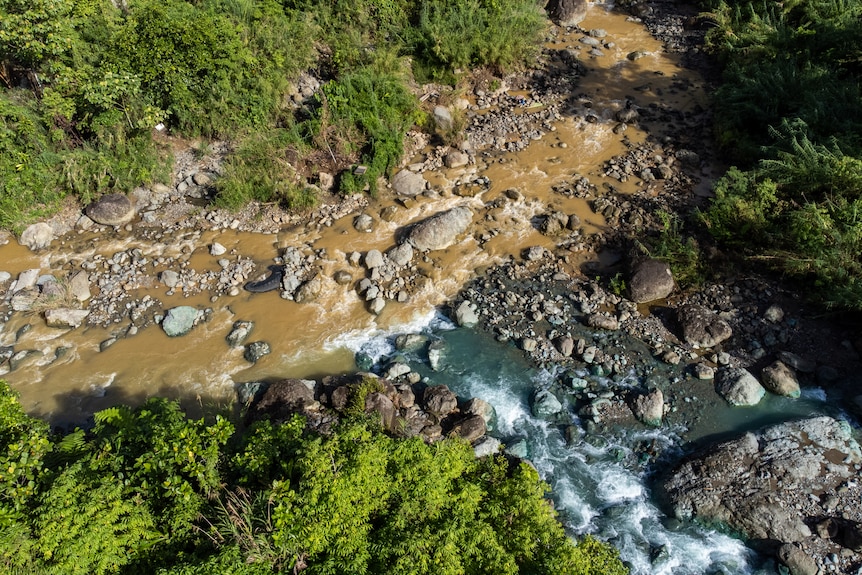 A birds eye view of a flowing brown coloured river meeting with a blue tinged river.