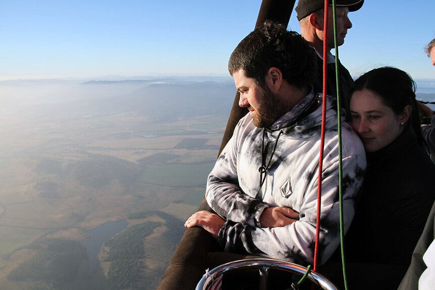Two people look out from a hot air balloon over Tasmania.