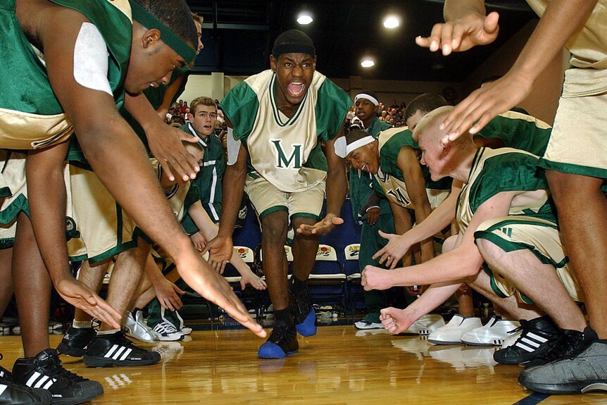 a young LeBron James in his high school basketball uniform walks on to the court as his teammates stretch out their hands