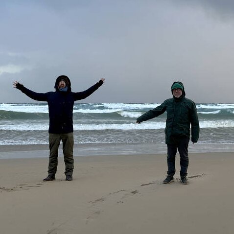 two cold men on a beach raising their arms in excitement