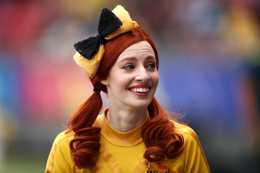 Woman wearing a red wig and yellow shirt smiles. 