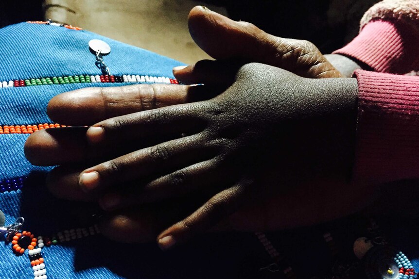 A close-up shows midwife Salune Laton Koikai holding hands with her granddaughter.