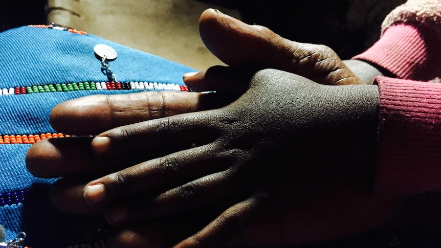 A close-up shows midwife Salune Laton Koikai holding hands with her granddaughter.